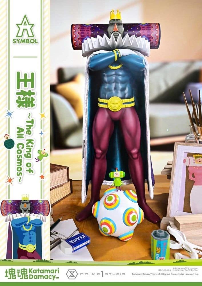The King of All Cosmos statue stands with his arms folded behind the Prince statue, who rides his katamari on a desk